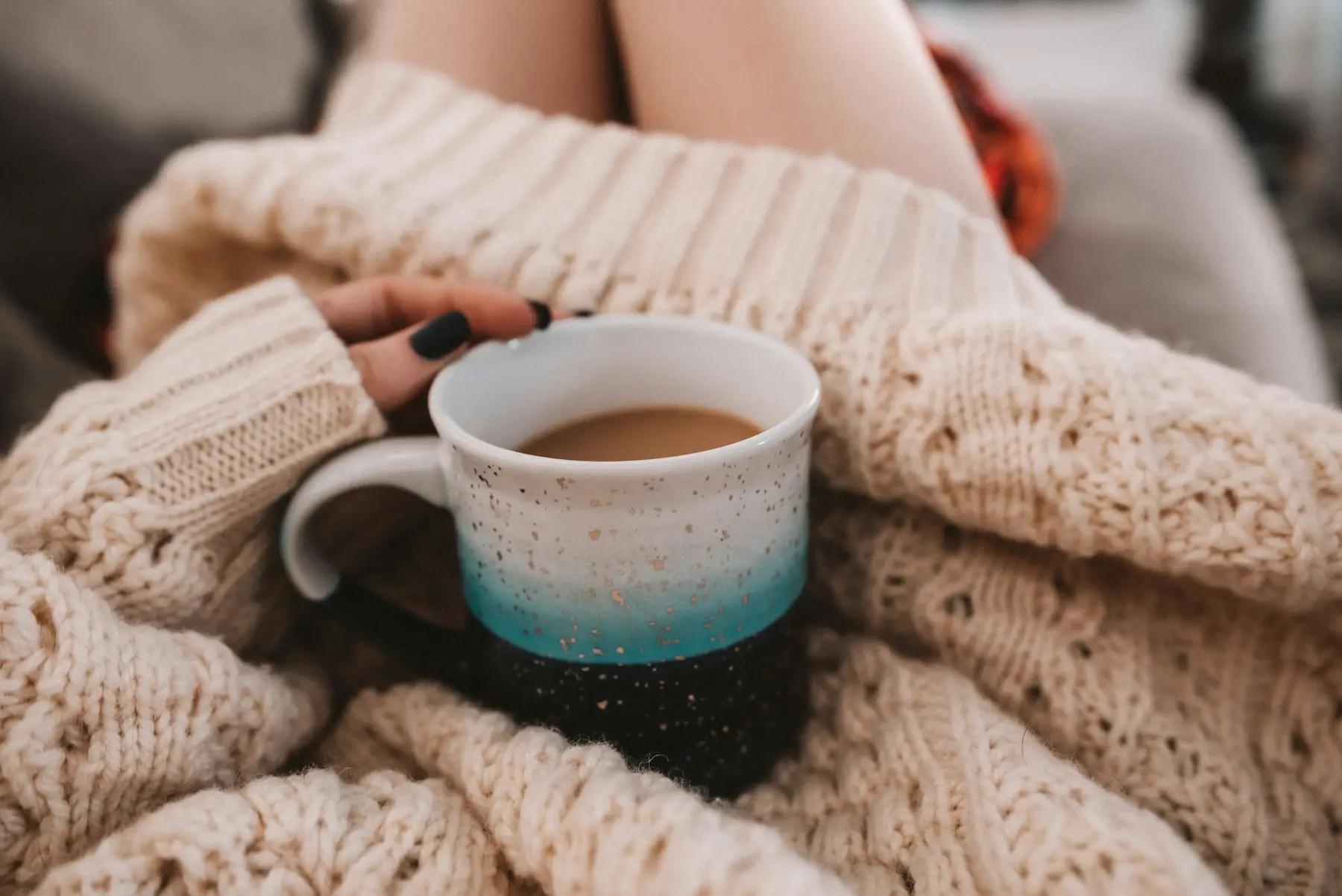 Hands holding a mug of coffee wrapped in a cream knit sweater