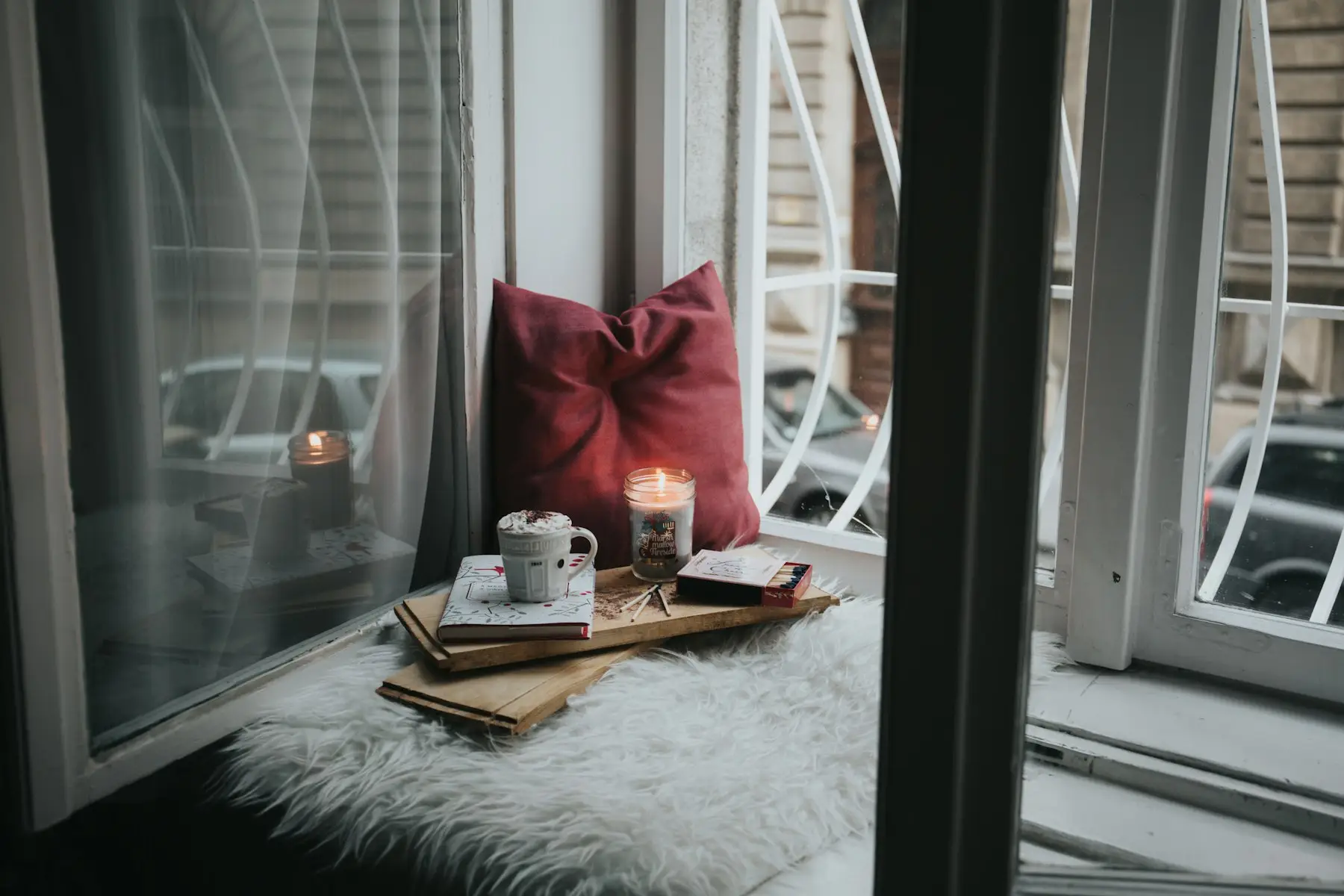Window seat with a sheepskin, cushions, books and a candle